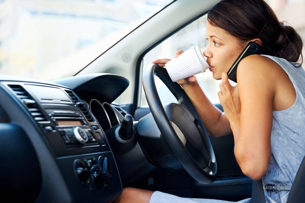 Businesswoman multitasking while driving, drinking coffee and talking on the phone