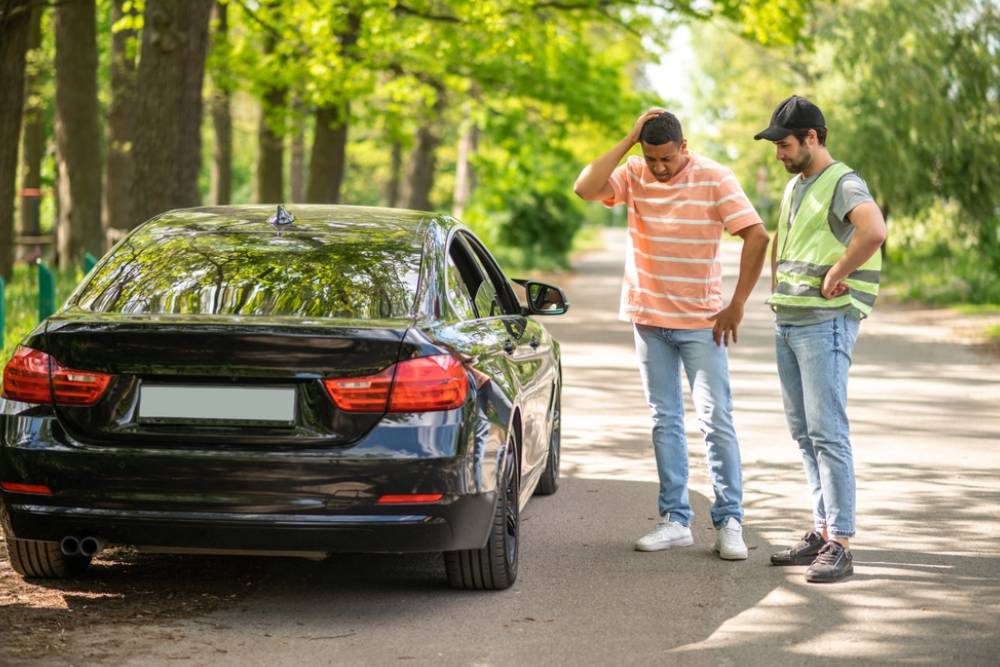 A driver discussing a car accident with a service man and looking uncertain