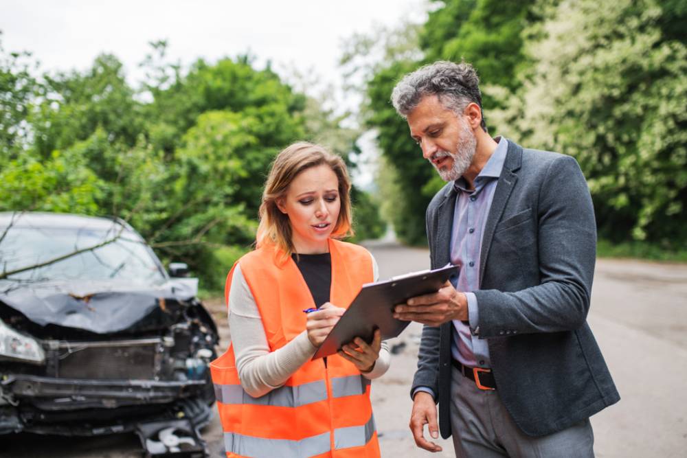 An insurance agent talking to a woman outside on the road after a car accident.