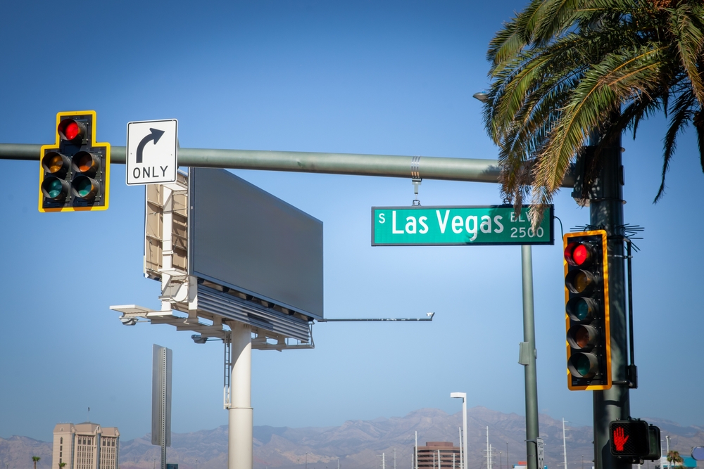 A typical American intersection on Las Vegas Boulevard (or las vegas strip), featuring traffic lights, road signs, and palm trees